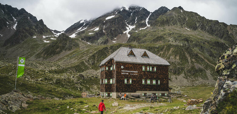 Hochschober Huette Ein Mann mit roter Jacke steht vor der Hochschober Huette an einem bewölkten Tag.