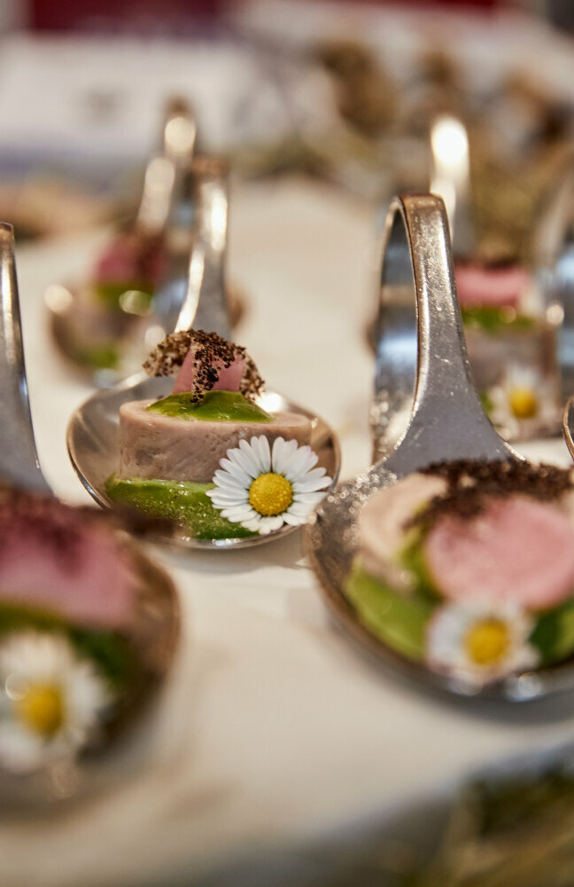 Haubenküche im Gannerhof - Gericht bestehend aus einem runden Fleischstück mit einer grünen Soße verziert mit einem Gänseblümchen auf einem Löffel angerichtet.