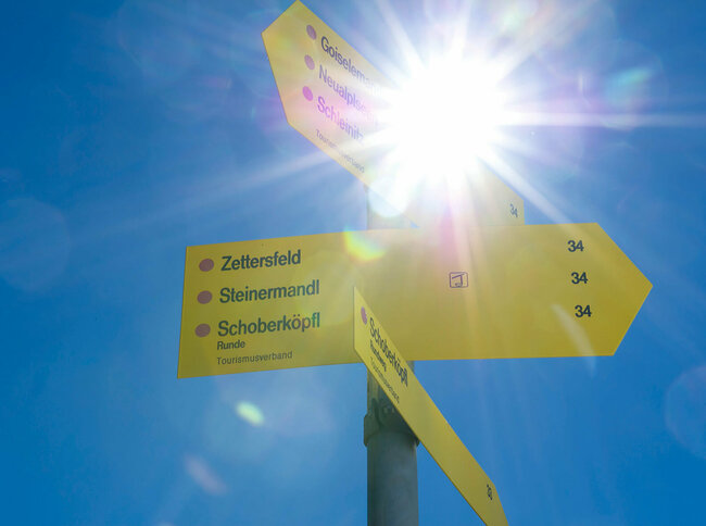 Zettersfeld wandern Ein gelber Wegweiser zur Orientierung am Zettersfeld steht von der Sonne geblendet im blauen Himmel.