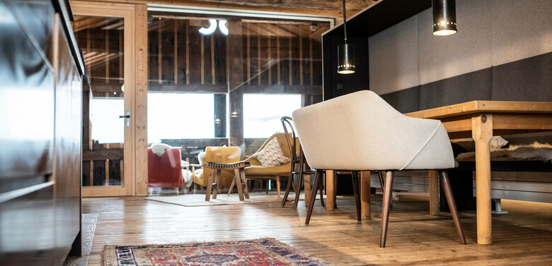 Innenansicht der Ferienwohnung Bergsteiger SEIN im Kesslerstadel aus der Ameisenperspektive mit einem gemusterten Teppich auf dem Holzboden, einem Esstisch mit gepolsterter Bank und Wintergarten mit gemütlichen Stühlen.