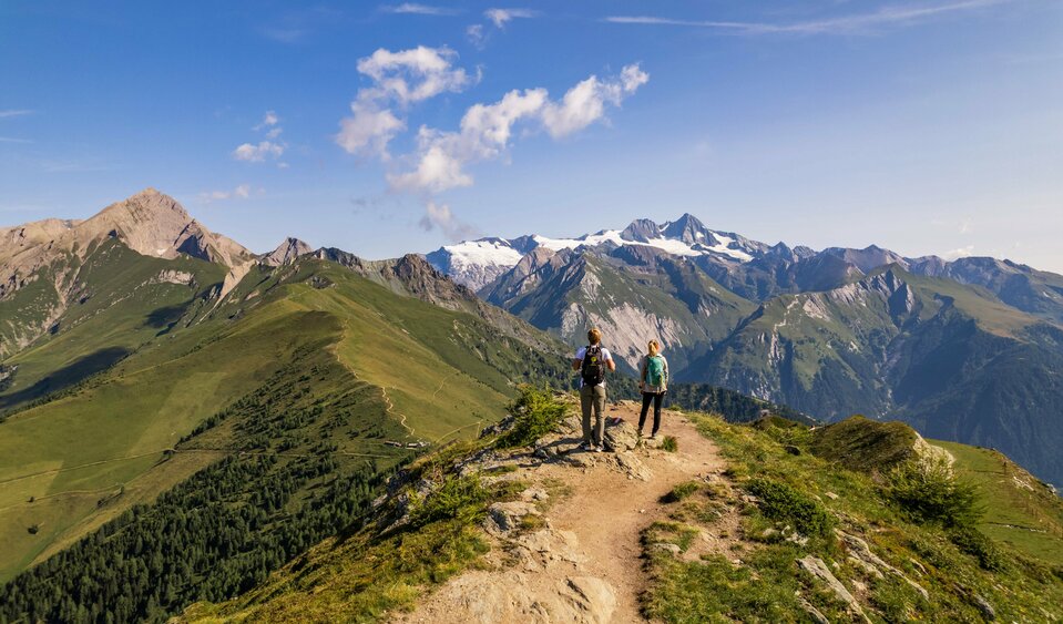 Zwei Frauen stehen auf einem schmalen Weg auf der Hoch und Heilig Etappe 8 in Kals und blicken in die Bergwelt auf und um den Großglockner.