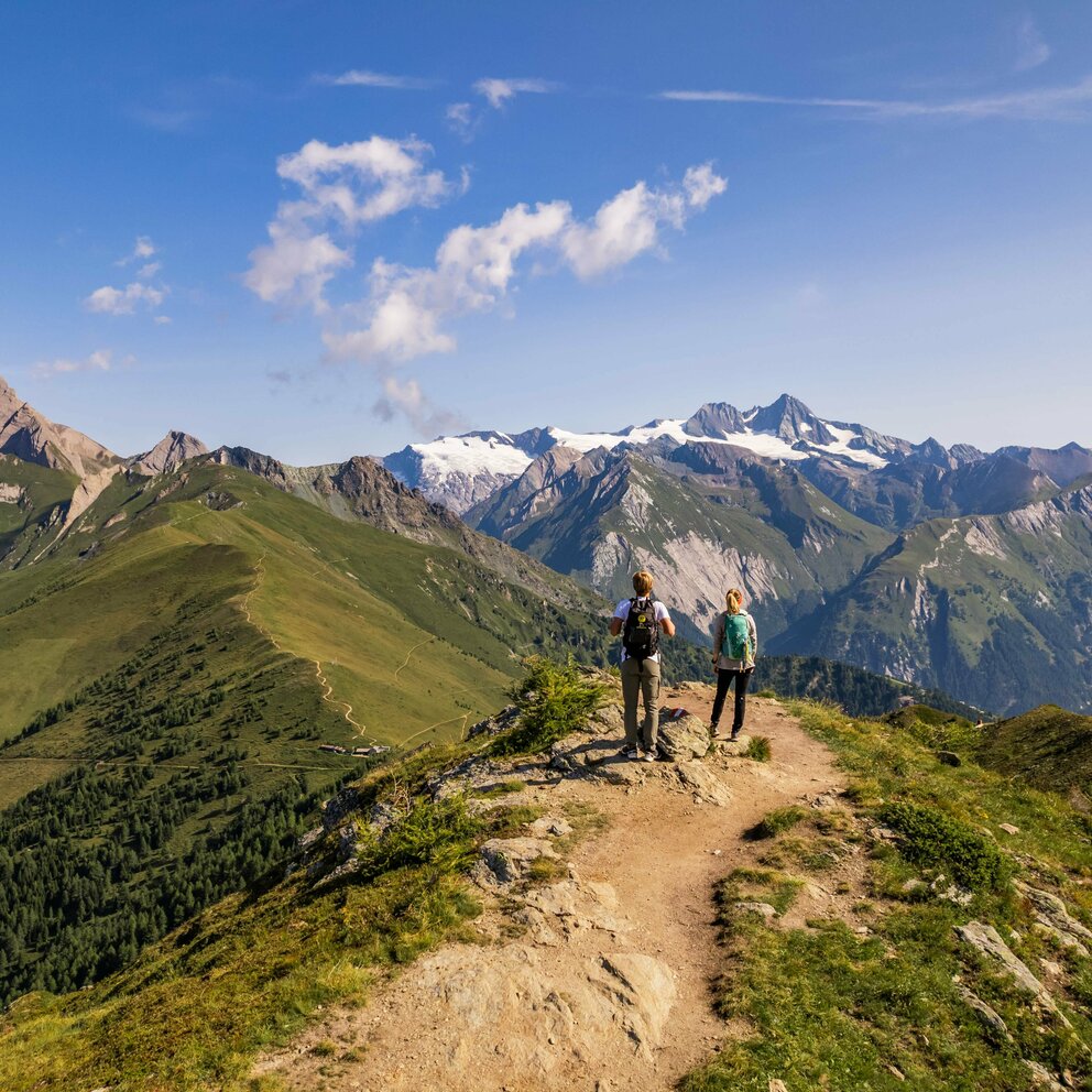 Zwei Frauen stehen auf einem schmalen Weg auf der Hoch und Heilig Etappe 8 in Kals und blicken in die Bergwelt auf und um den Großglockner.
