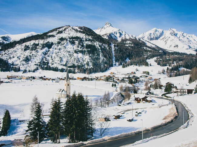Kals Blick auf das verschneite Kals mit Kirche und Wohnhäusern, an einem sonnigen Tag.