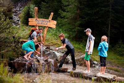 Wassererlebnis St. Jakob Eine Rangerin des Nationalpark Hohe Tauern bei einer Wanderung auf dem Wassererlebnisweg in St. Jakob i. D.. Gerade machen sie bei einer Wasserquelle Halt, um sich mit dem klaren Wasser zu erfrischen.