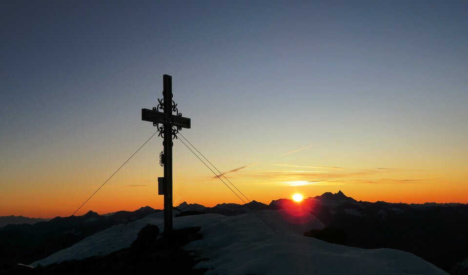 Sonnenaufgang auf der Weissspitze Sonnenaufgang am Gipfelkreuz der schneebedeckten Weissspitze. Der Himmel färbt sich in der Morgenröte und die Sonne erscheint langsam hinter der Bergkette.