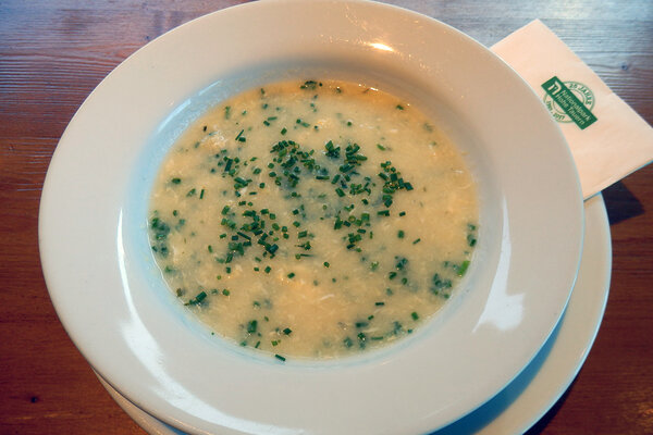 Ein weißer Teller mit legierter Griessuppe und Kräutern.