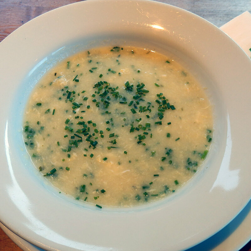 Ein weißer Teller mit legierter Griessuppe und Kräutern.