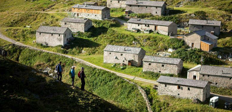 Drei Wanderer blicken auf die Steingebäude der Jagdhausalmen im Nationalpark Hohe Tauern.