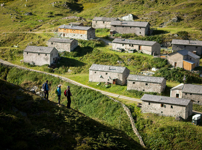 Drei Wanderer blicken auf die Steingebäude der Jagdhausalmen im Nationalpark Hohe Tauern.