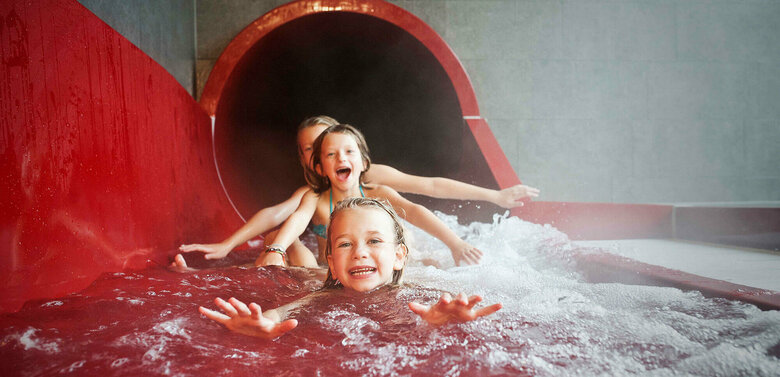 Drei Mädchen am Ausgang einer roten Wasserrutsche im Dolomitenbad in Lienz.