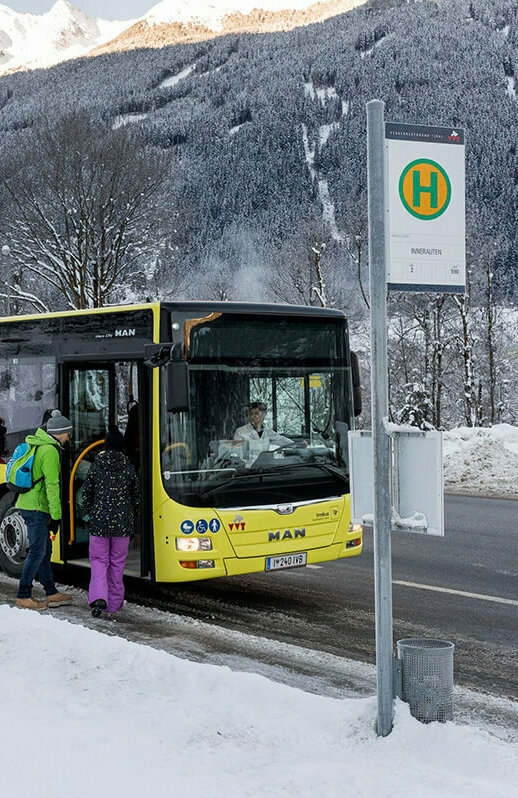 Gelber Bus hält an einer Bushaltestelle im Winter und lässt Fahrgäste ein- und aussteigen.