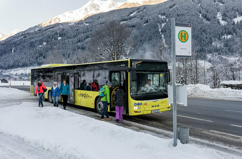 Gelber Bus hält an einer Bushaltestelle im Winter und lässt Fahrgäste ein- und aussteigen.