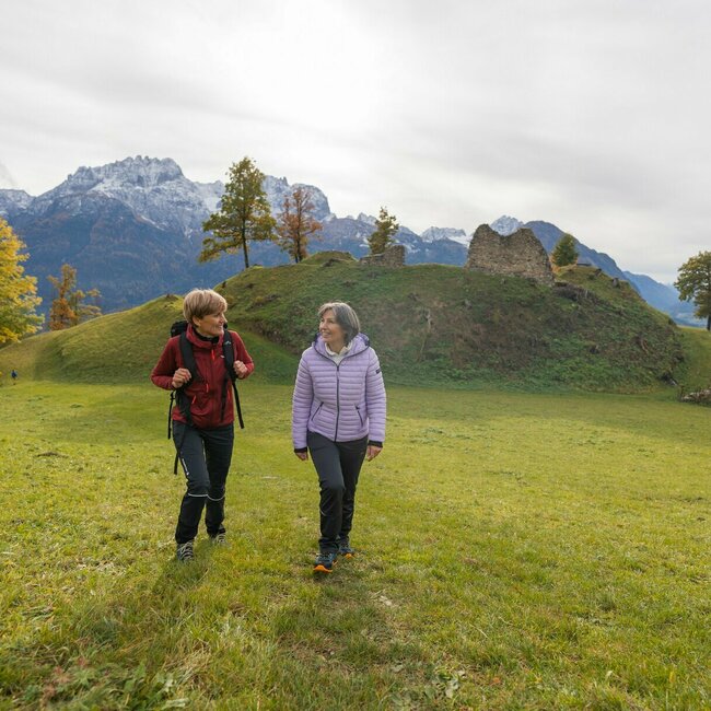 Hiking Walchenstein ruins Two ladies walk across a green meadow and smile at each other. The Walchenstein ruins can be seen in the background.