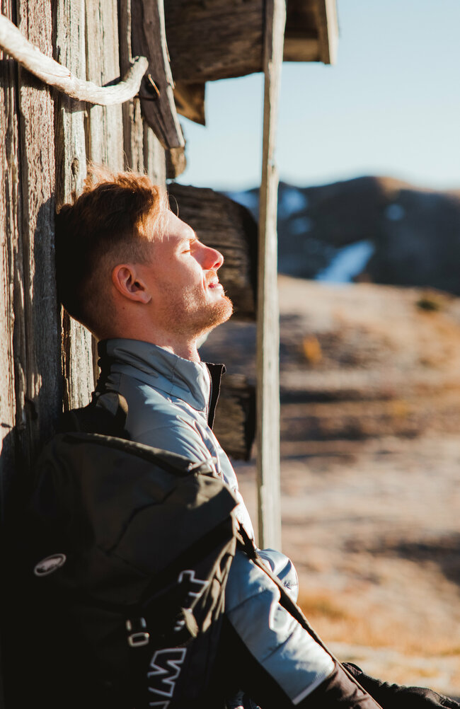 Wanderer genießt die wärmende Sonne bei einer alten Heuhütte der Kutteschupfen