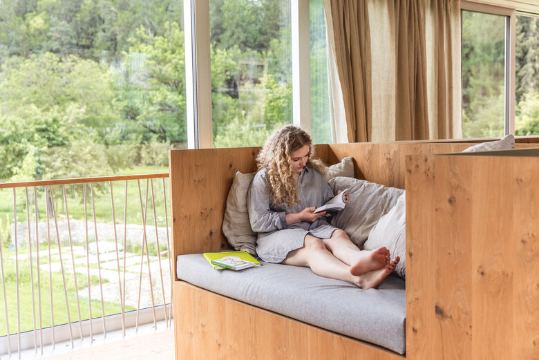 Frau entspannt auf dem Sofa in ihrer Unterkunft und blättert in einem Buch.