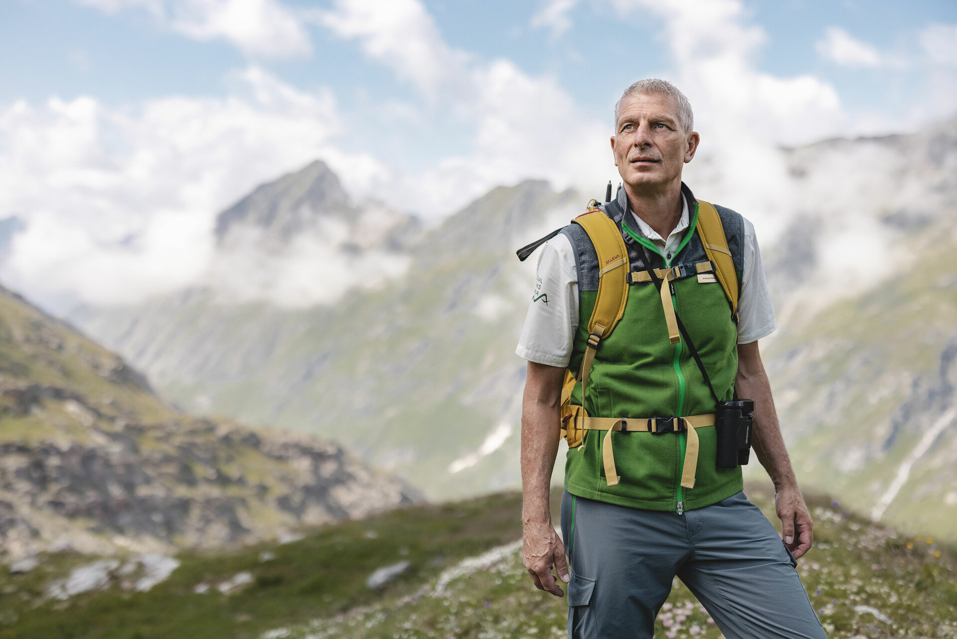 Ein Ranger des Nationalpark Hohe Tauern mit grüner Weste steht im Gschloesstal und blickt in die Bergwelt.