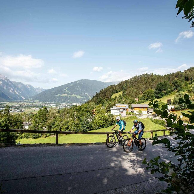 Nussdorf Zwei Radfahren fahren eine asphaltierte Straße bergauf, mit Blick auf Nussdorf Debant und den Lienzer Talboden.
