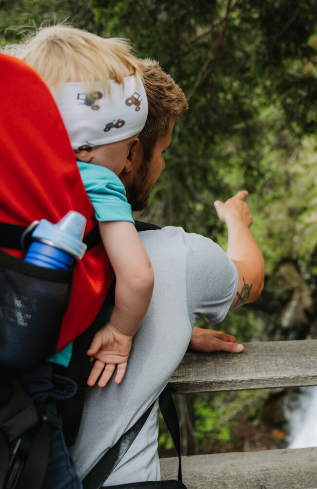 Wasserfall Familienwanderung Kristeinertal Ein Mann mit einem kleinen Kind auf dem Rücken zeigt einem Mädchen den Wasserfall im Kristeinertal.