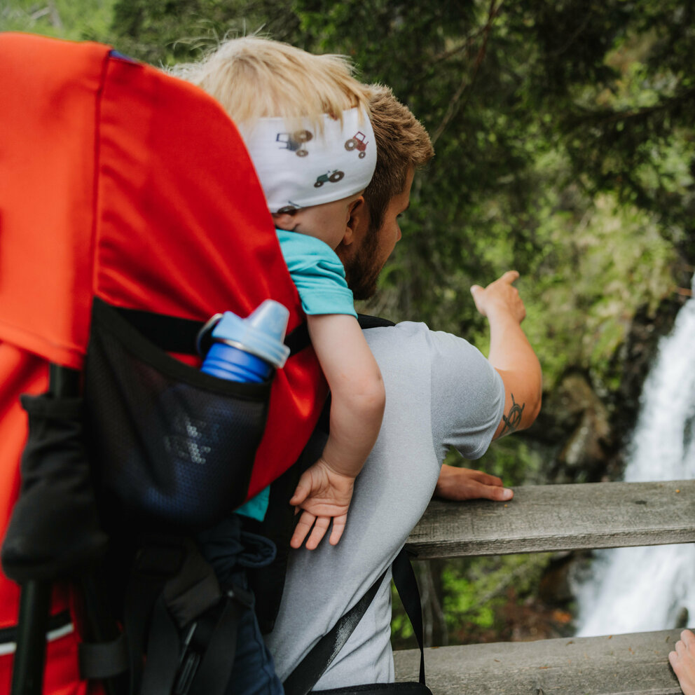 Wasserfall Familienwanderung Kristeinertal Ein Mann mit einem kleinen Kind auf dem Rücken zeigt einem Mädchen den Wasserfall im Kristeinertal.