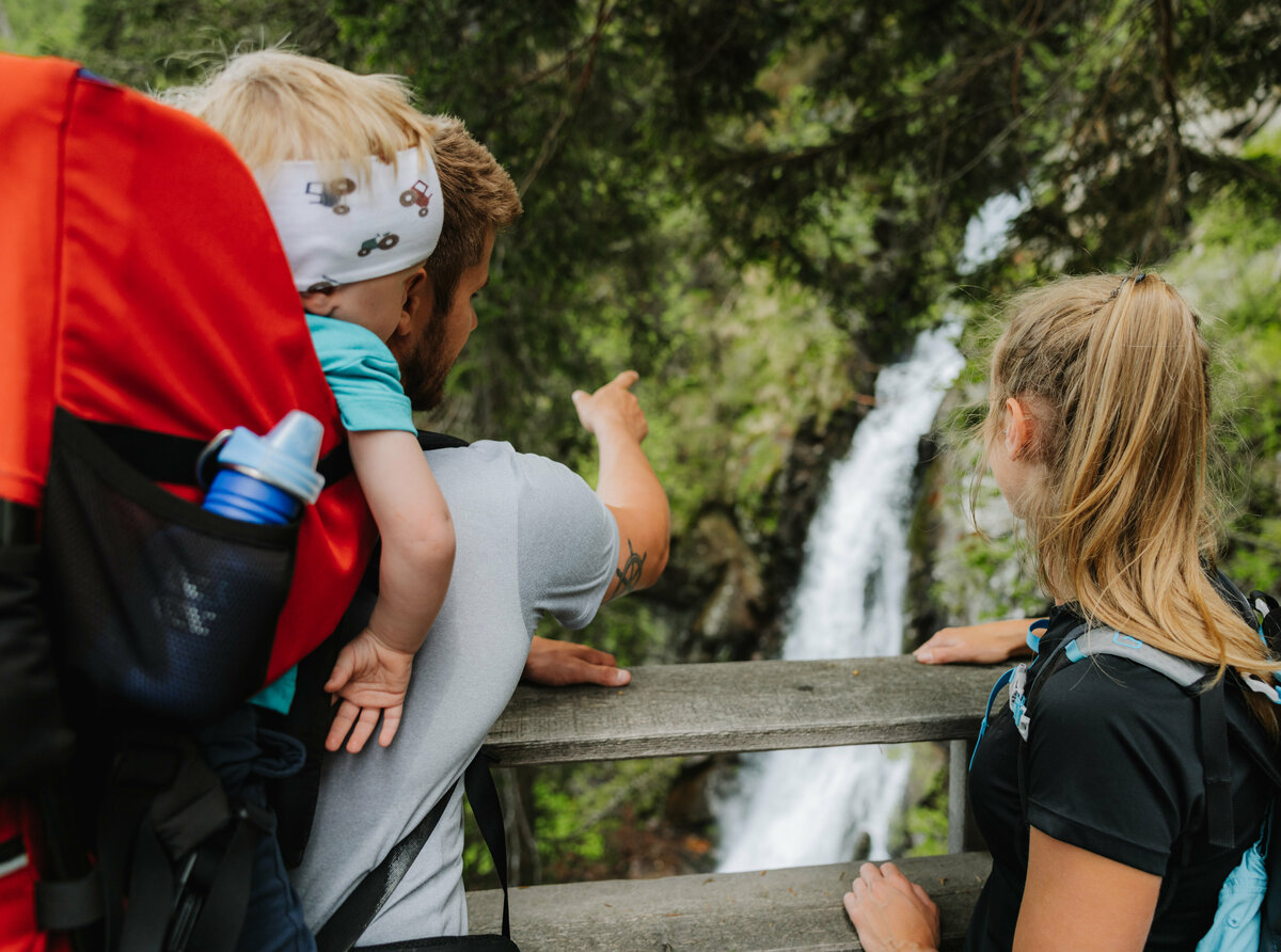 Wasserfall Familienwanderung Kristeinertal Ein Mann mit einem kleinen Kind auf dem Rücken zeigt einem Mädchen den Wasserfall im Kristeinertal.