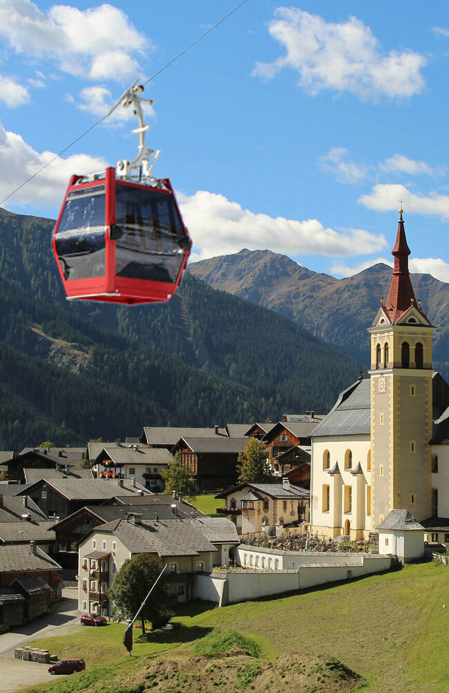 Sommergondel der Obertilliach Bergbahn fährt am Tal und der Kirche Obertilliachs vorbei