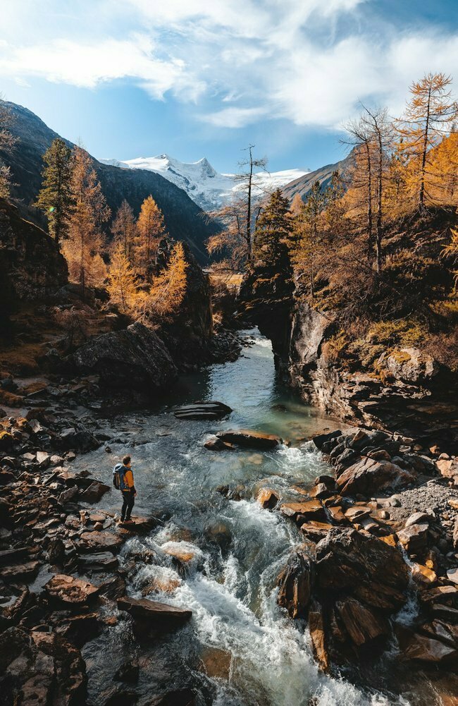Wanderer in herbstlicher Landschaft im Gschlösstal bei einem Bach mit schneebedeckten Gipfel im Hintergrund.