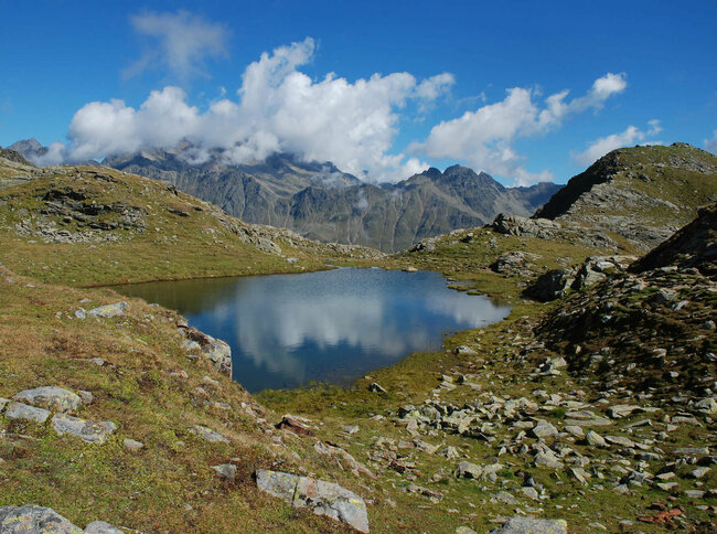 Neualpenseen Zettersfeld Einer der Neualpenseen am Lienzer Zettersfeld, im Vordergrund der klare Bergsee, im Hintergrund ein mächtiges Bergmassiv unter blauem Himmel.