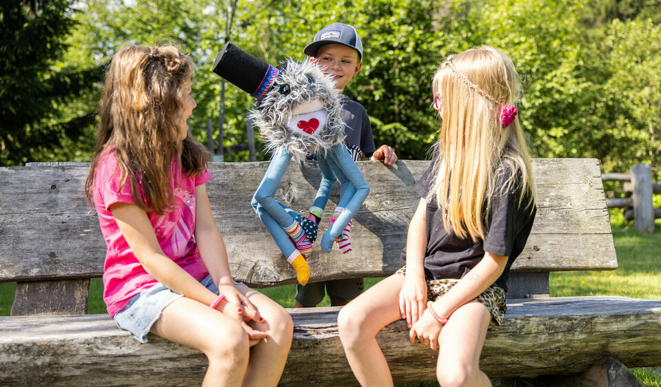 Kinder sitzen mit Spinne Spinnfried Maskottchen auf einer Bank