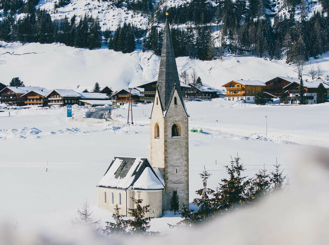 Kals Kirche Die Kals Kirche mit dunklem Kirchturm liegt von Schnee bedeckt vor dem Dorf.