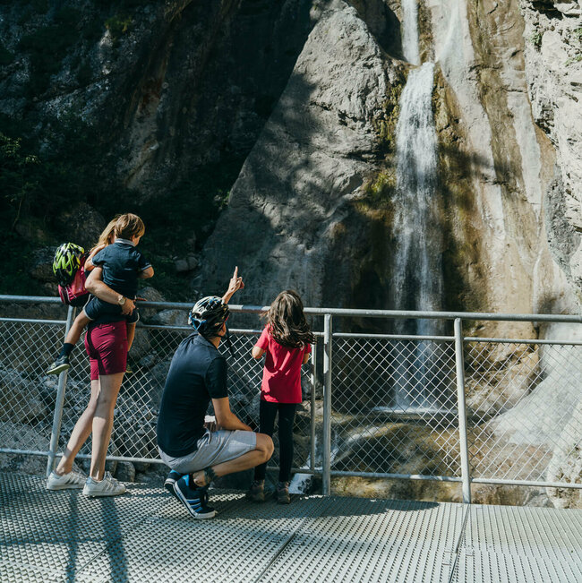 Frauenbach Wasserfall Lavant Eine vierköpfige Familie steht auf der Plattform des Frauenbachwasserfalls in Lavant. Ein Rundwanderweg, auch "Waldpfad" genannt, führt direkt an diesem Naturjuwel vorbei.