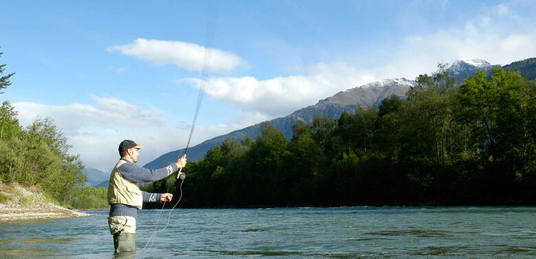 Ein Mann steht in einem Fluss und wirft seine Angel aus zum Fliegen fischen.