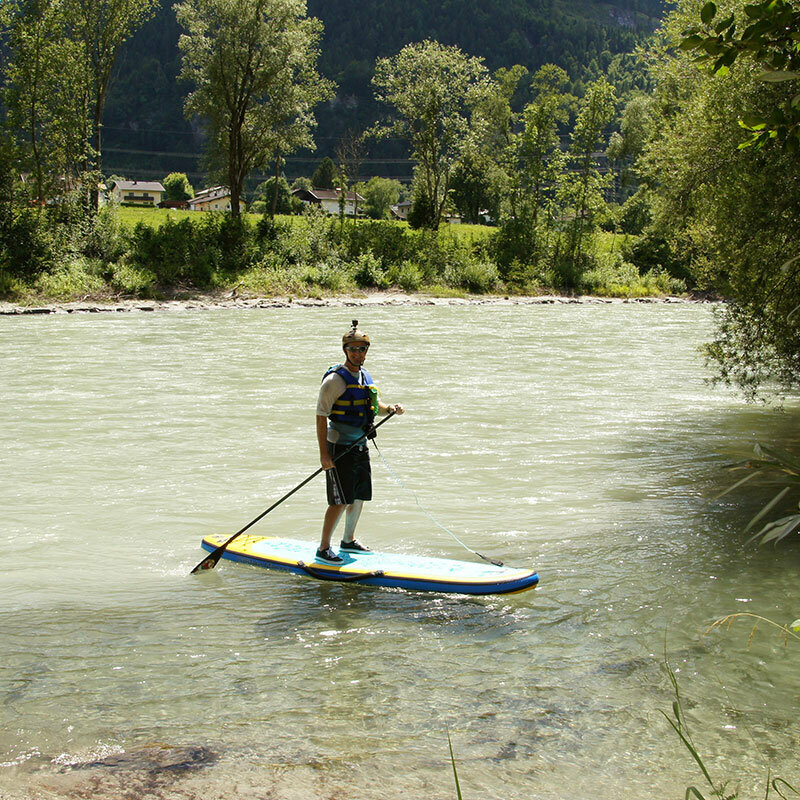Eine Person mit Schwimmweste und Helm steht auf einem Stand Up Paddle Board auf der Isel.