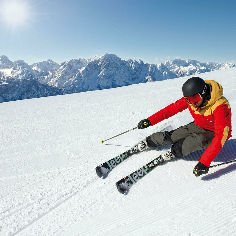Terrassenskilauf Zettersfeld Skifahrer mit rot-gelber Jacke und schwarzem Helm beim Terrassenskilauf am Zettersfeld Skigebiet. Die Sonne strahlt und der Himmel ist blau.