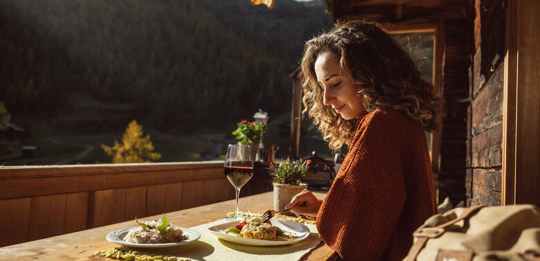 Herbst ist Genusszeit! Von edlen Restaurants bis zu urigen Hütten wie hier auf der Unterstaller Alm. Eine Frau genießt eine Portion Schlipfkrapfen auf der Terasse der Unterstaller Alm