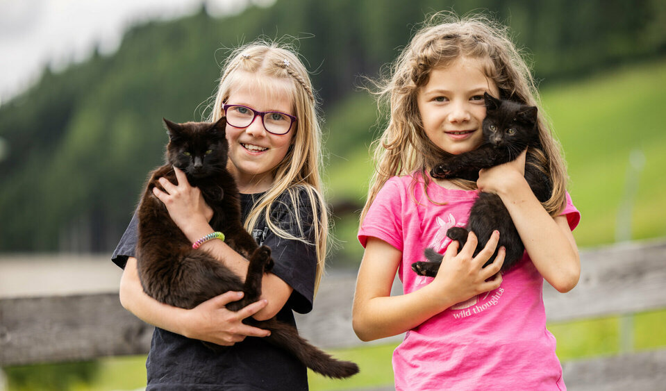 Zwei Mädchen haben eine schwarze Katze im Arm