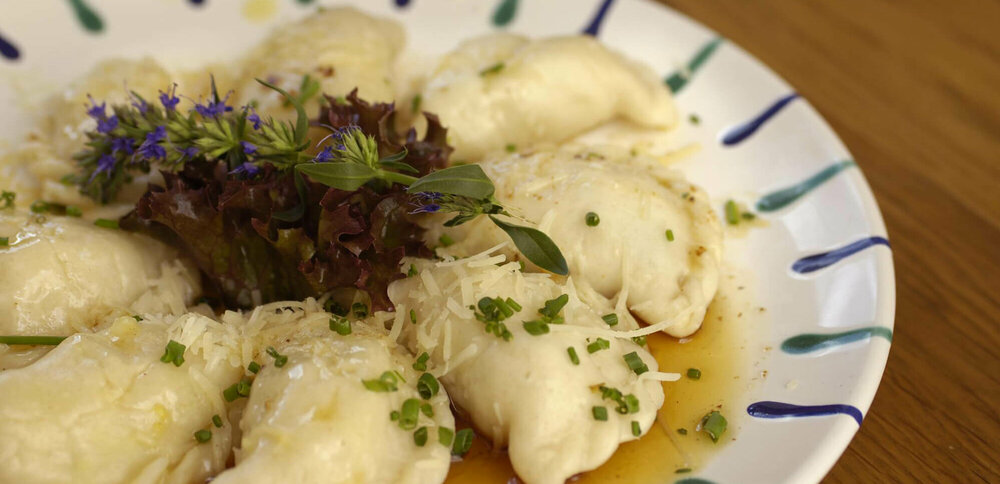 Ostiroler Schlipfkrapfen Osttiroler Schlipfkrapfen mit Schnittlauch und geschmolzener Butter auf einem weiß-blauen Teller, mit etwas Salat verziert.