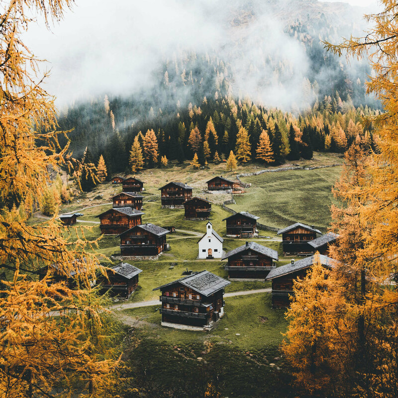Almhüttendorf "Oberstalleralmen in Innvervillgraten" in herbstlicher Umgebung mit kleiner Kapelle im Zentrum; im Vordergrund goldgelbe Lärchen in Herbstfärbung