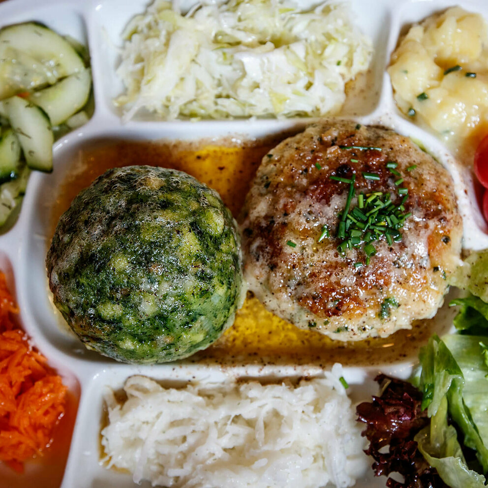 Spinatknödel und Kaspressknödel in brauner Butter. Ringsherum verschiedene bunte Salate auf einem Teller angerichet.