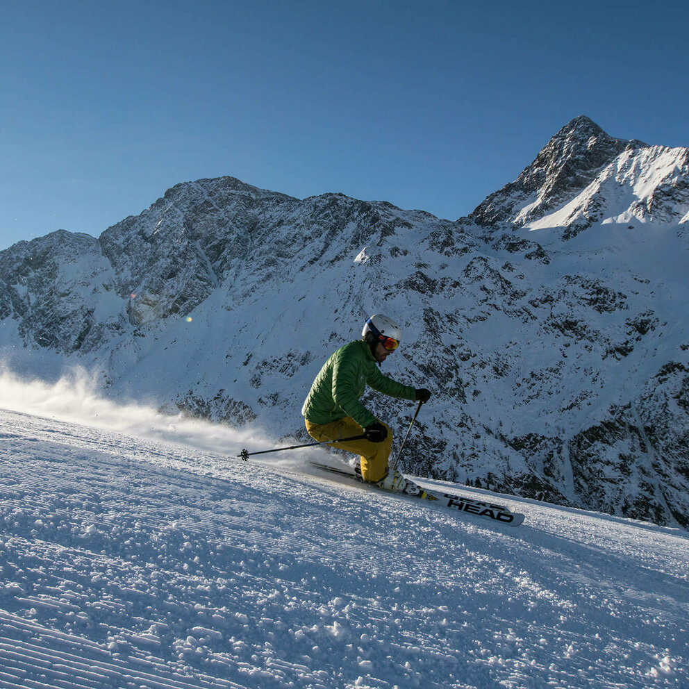 Skizentrum St. Jakob Ein Skifahrer mit grüner Jacke und gelber Hose fährt in sportlichem Fahrstil auf der Abfahrt in Skizentrum St. Jakob im Defereggen.
