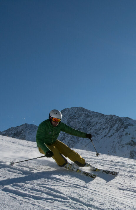 Ein Skifahrer mit grüner Jacke und gelber Hose carvt über die Pisten im Skizentrum St. Jakob im Defereggental bei Kaiserwetter.