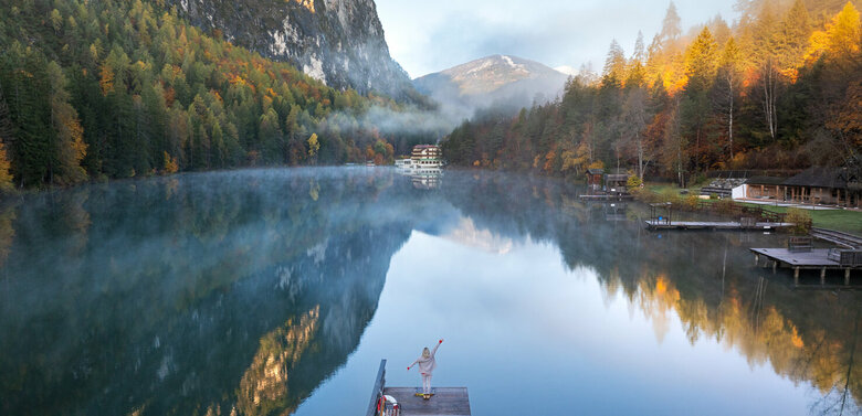 Das klare Wasser des Tristachersees im Herbst spiegelt die verfärbten Wälder und den Berghang rund um den See perfekt wider.