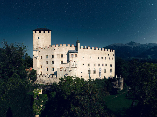 Aussenaufnahme bei Nacht von Schloss Bruck in Lienz mit Bergkulisse und Sternenhimmel im Hintergrund.