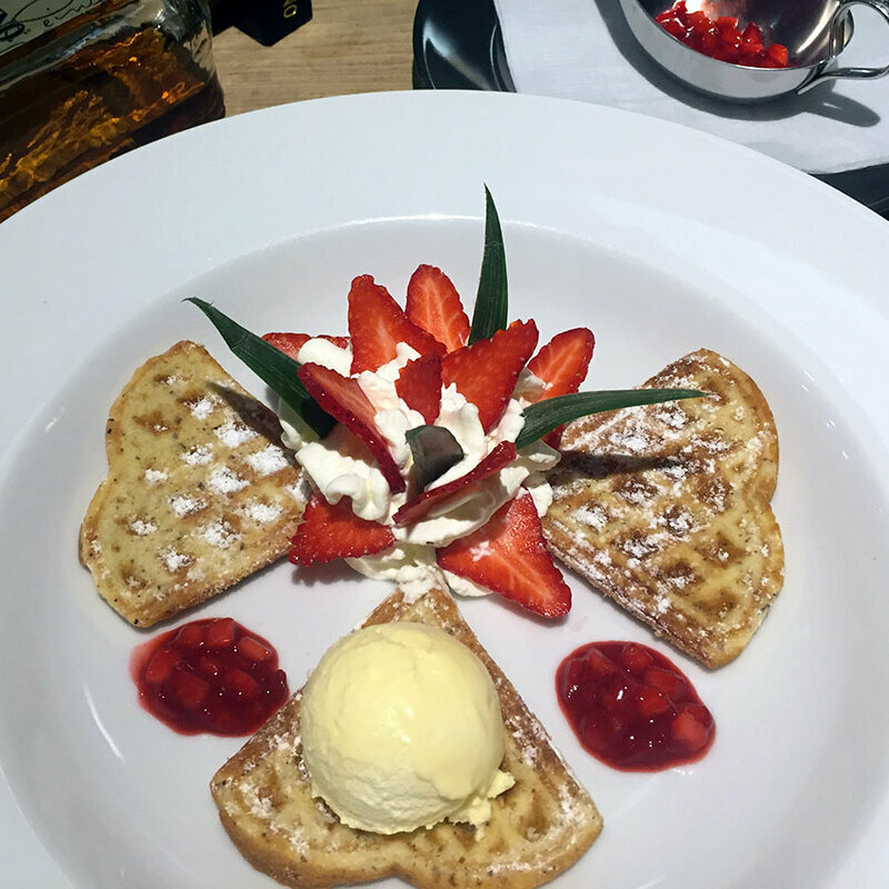 Drei Waffeln mit Erdbeeren, Sahne und einer Eiskugel auf einem Teller.
