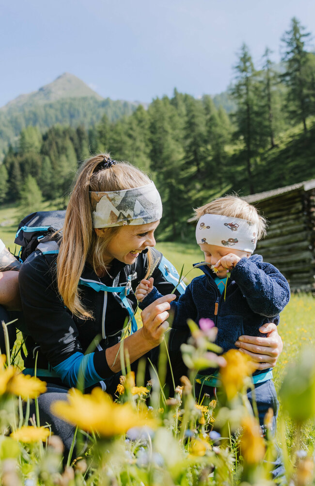 Wiese Familienwanderung Kristeinertal Eine kleine Familie ist im Zuge einer Familienwanderung auf einer Wiese im Kristeinertal. Die Frau und das Kind tragen Stirnbänder und der Mann hat einen roten Trage-rucksack auf dem Rücken. Sie sitzen im grünen Gras.
