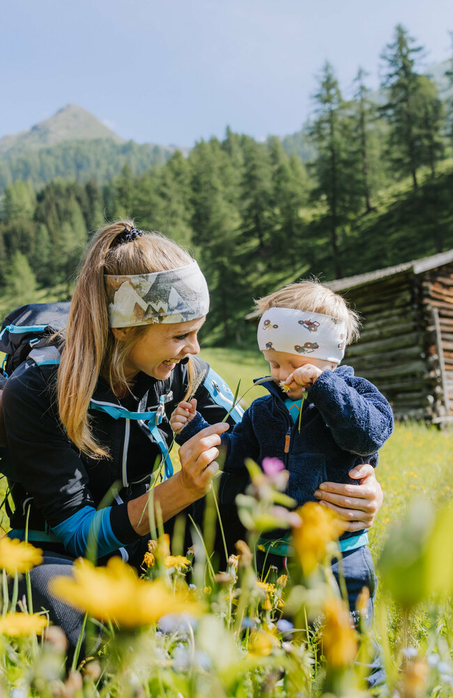 Wiese Familienwanderung Kristeinertal Eine kleine Familie ist im Zuge einer Familienwanderung auf einer Wiese im Kristeinertal. Die Frau und das Kind tragen Stirnbänder und der Mann hat einen roten Trage-rucksack auf dem Rücken. Sie sitzen im grünen Gras.