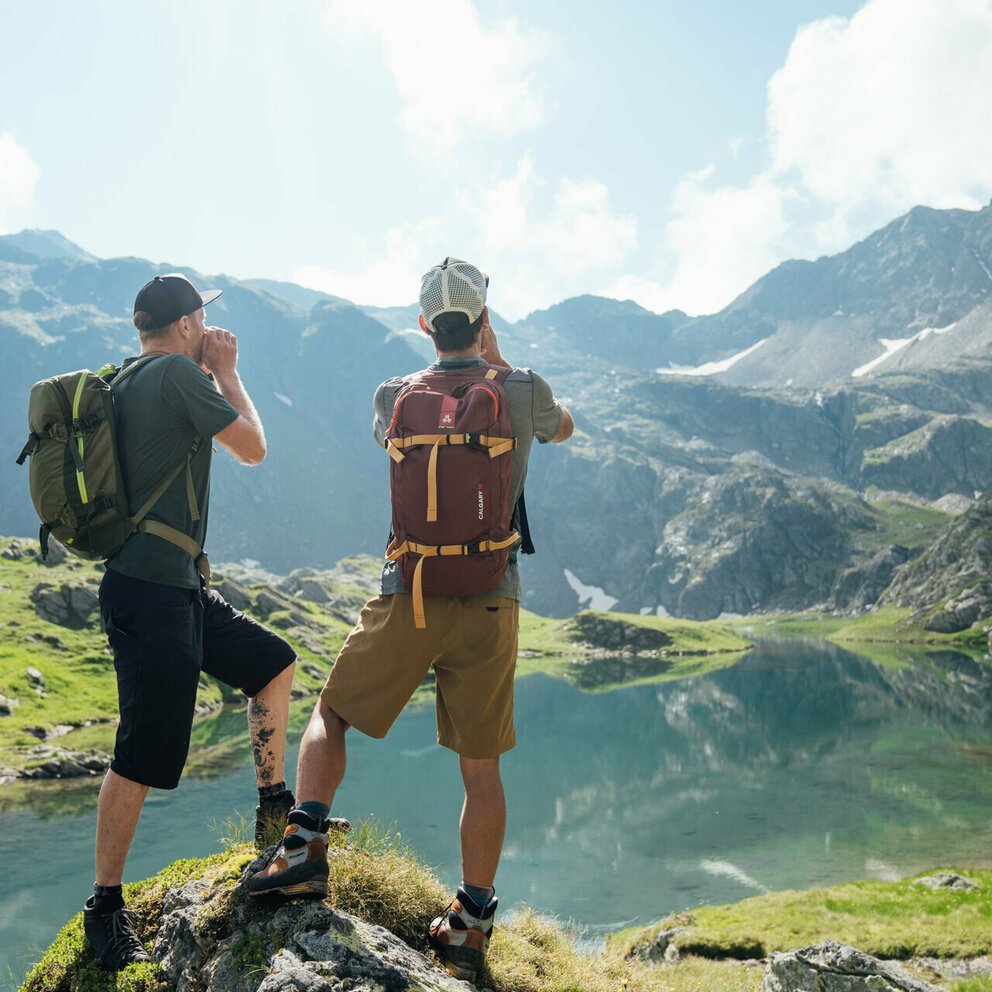 Zwei Wanderer stehen am Geigensee im Defereggental in Osttirol und rufen einen "Juchizer" aus.