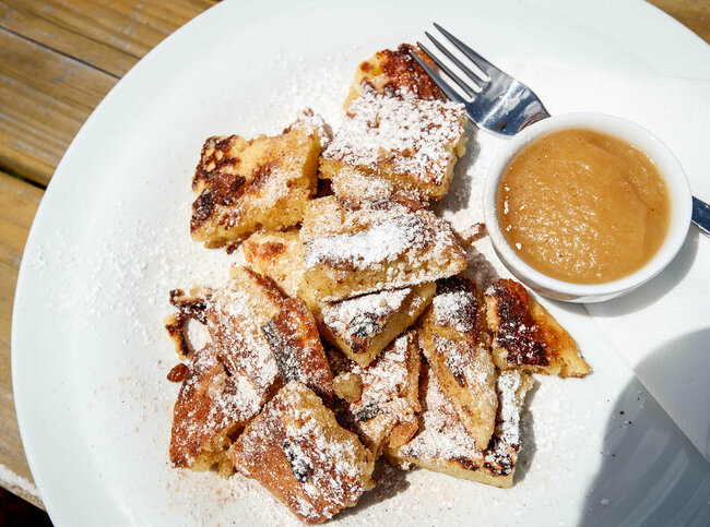 Kaiserschmarren mit Apfelmus in einem separaten Schüsselchen auf einem weißen Teller.