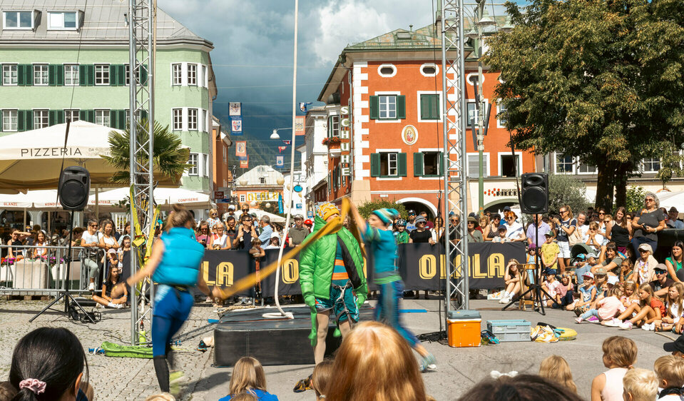 Drei Artistinnen am Olala 2025, zwei davon hüllen die dritte in dicke Winterkleidung, rundherum stehen und sitzen begeisterte Zuseherinnen und Zuseher.