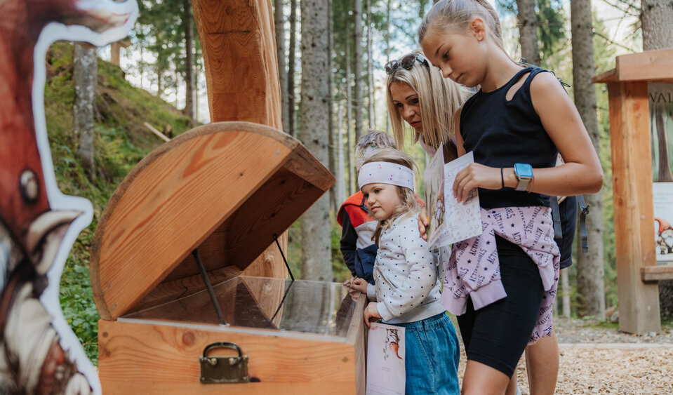 Eine Mutter und ihre zwei Töchter begutachten die Schatztruhe des Waldwichtelweges.