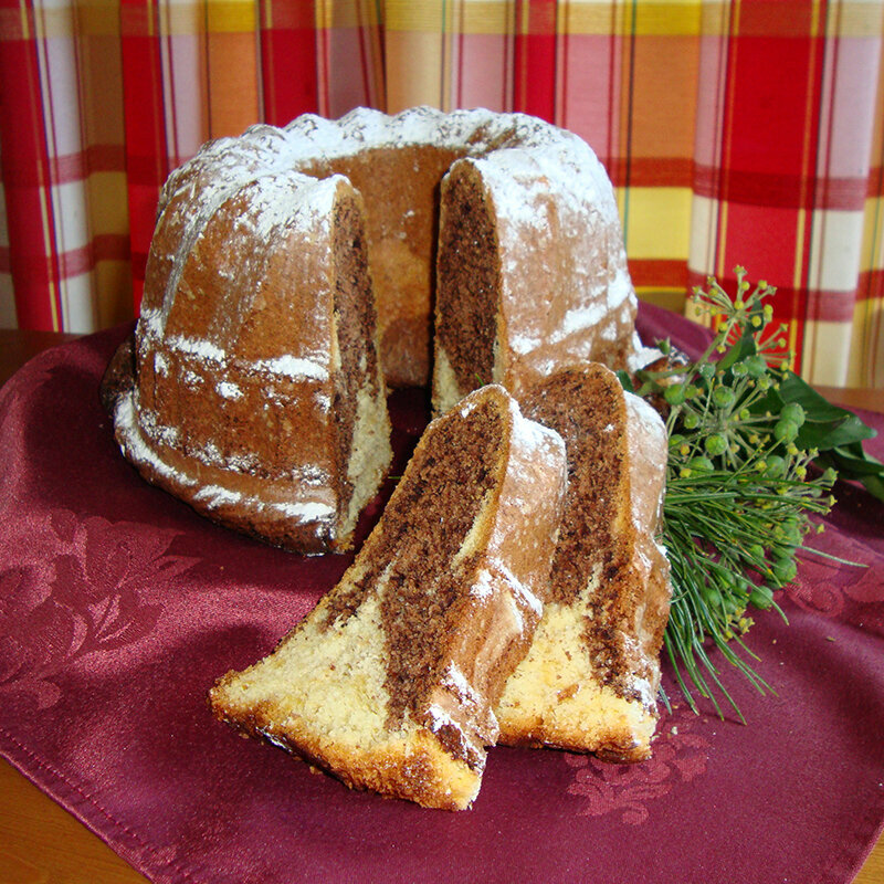 Ein ganzer Marmor-Gugelhupf mit zwei aufgeschnittenen Stücken davor.